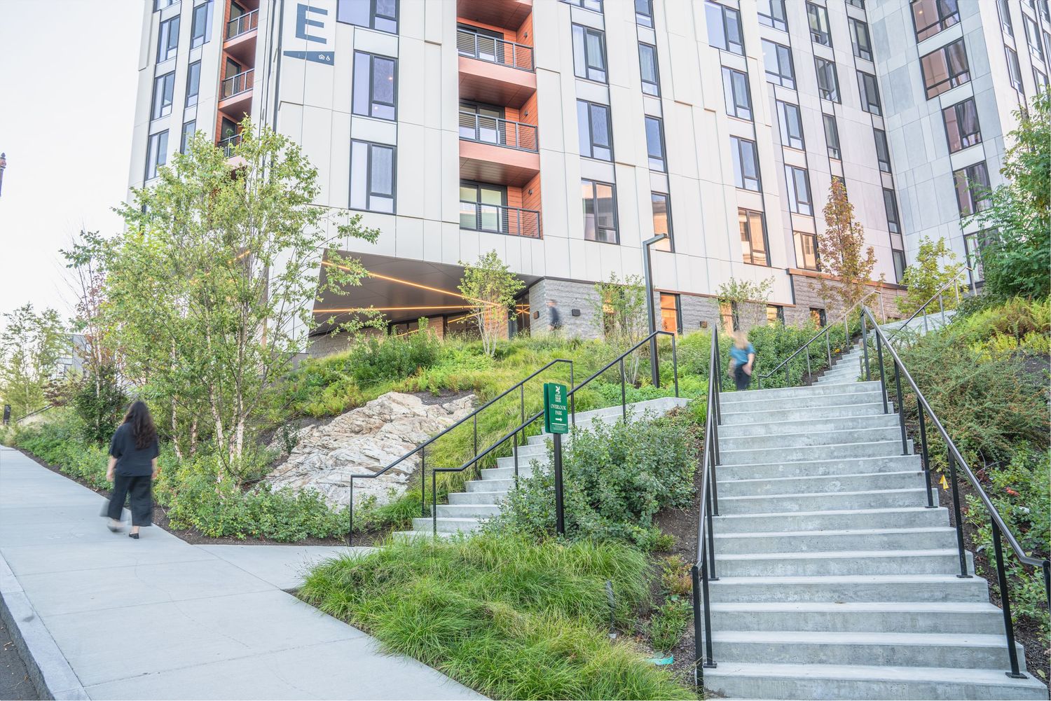 Concrete stairway with metal railings winding through a landscaped garden area near residential buildings.