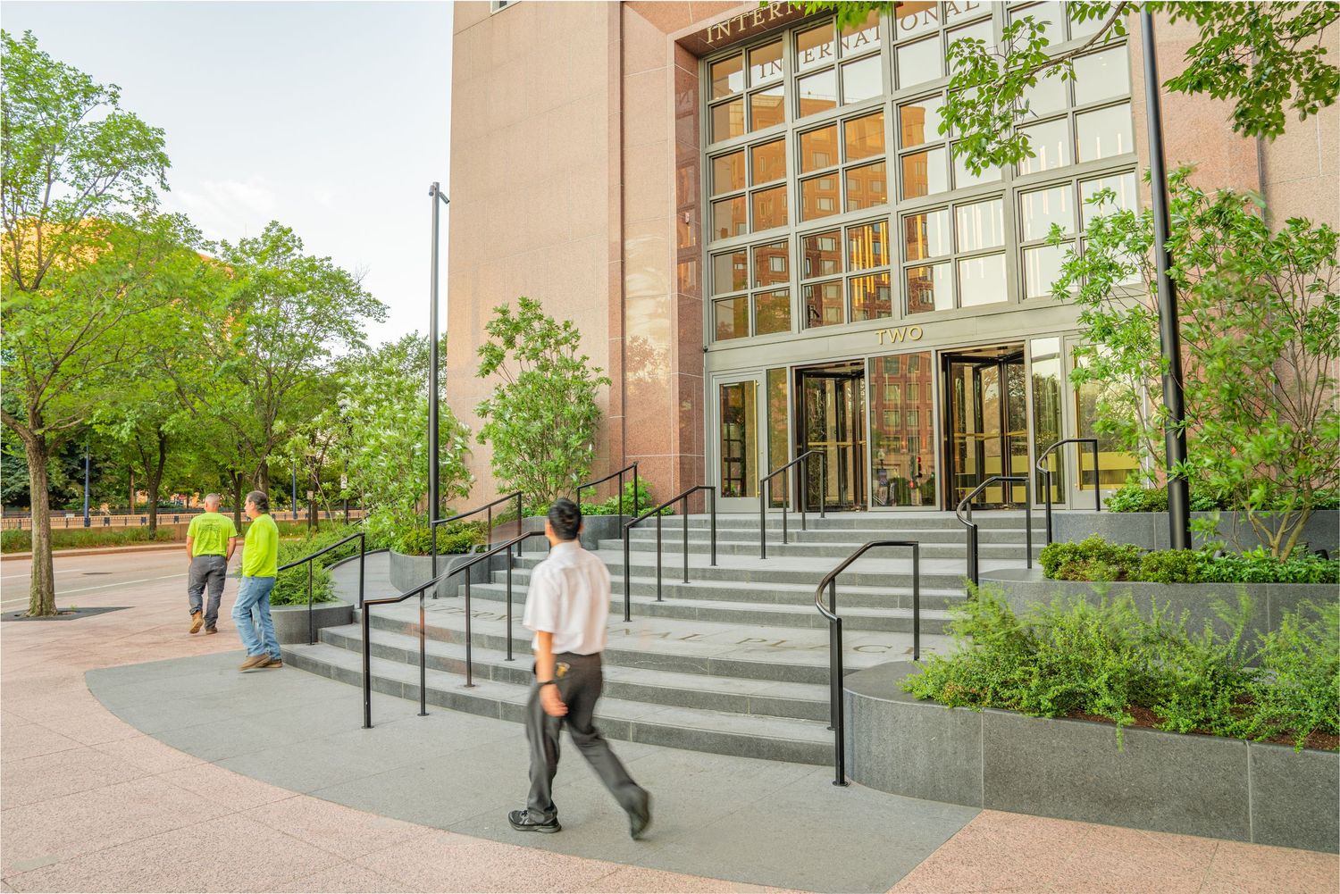 Stone steps with metal handrails leading to building entrance surrounded by greenery.
