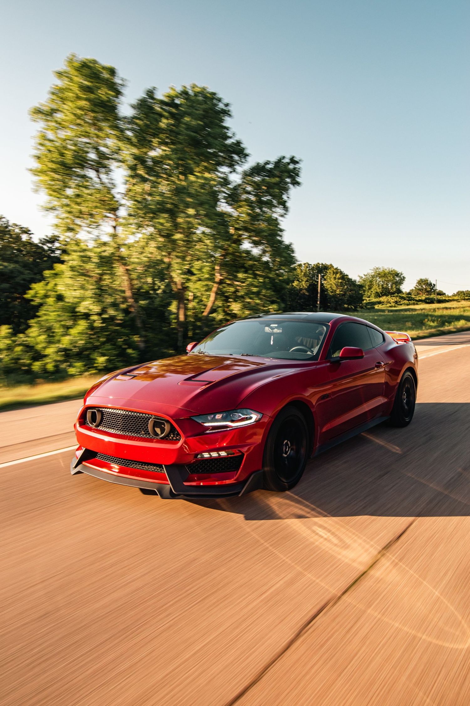 Dynamic rolling shot of a red Ford Mustang on the highway, captured in golden hour light with sleek lines and bold performance style.