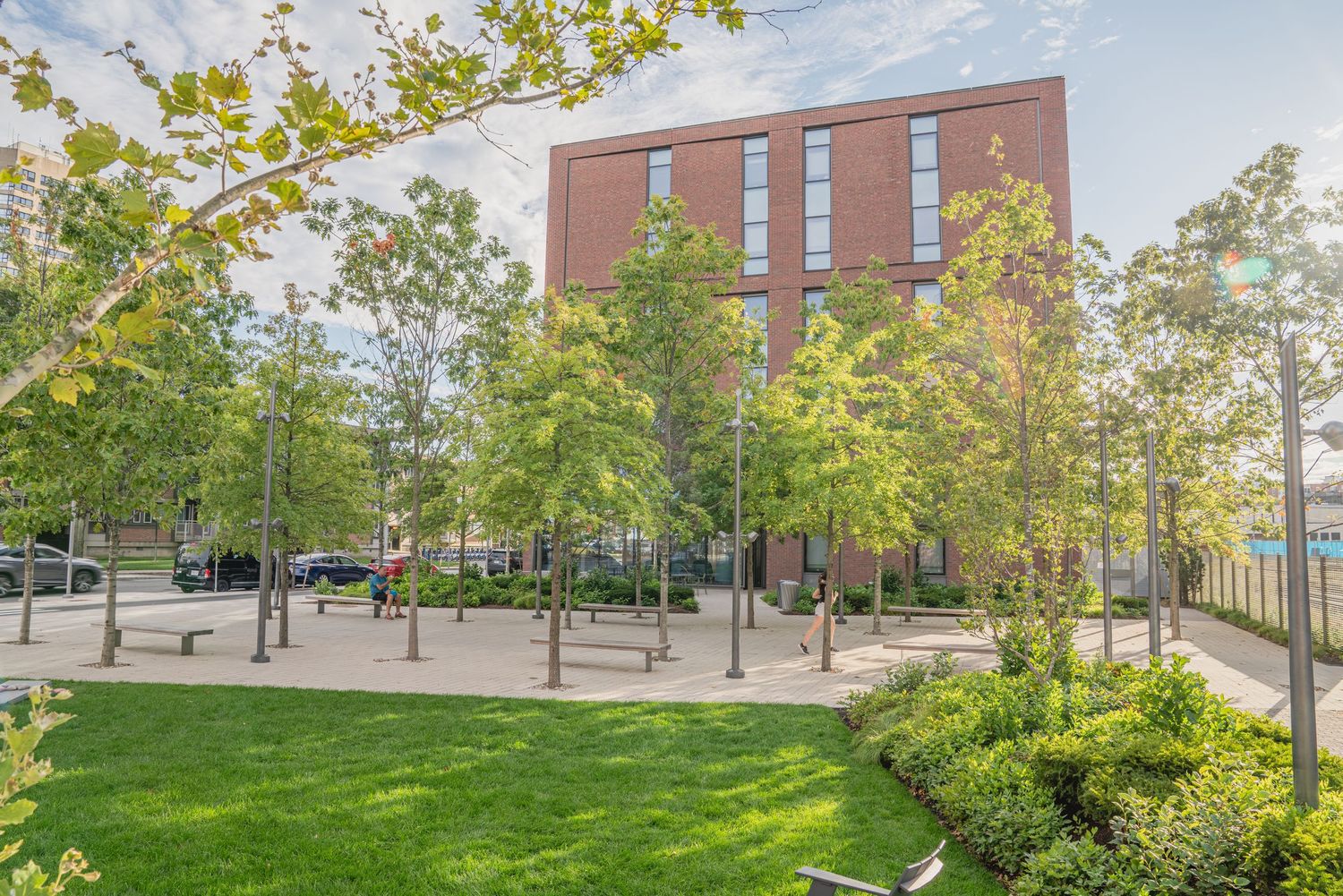 Contemporary urban plaza design with brick buildings, green lawns, and paved pathways.