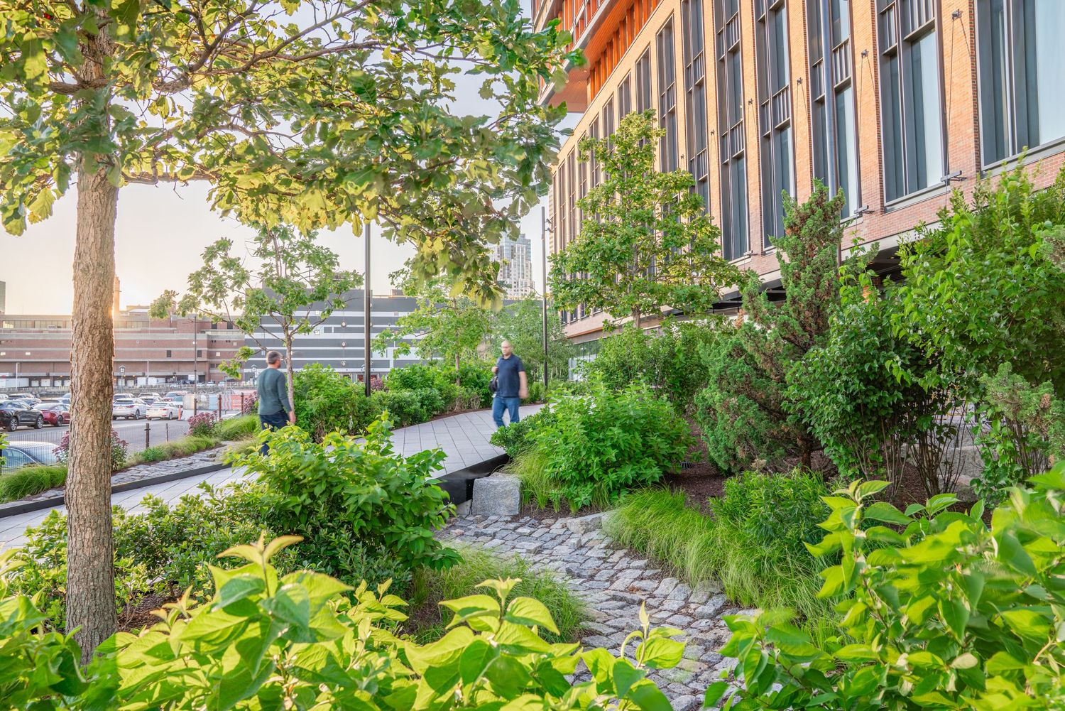 Modern urban landscaping features lush greenery and terraced gardens along a pedestrian walkway.