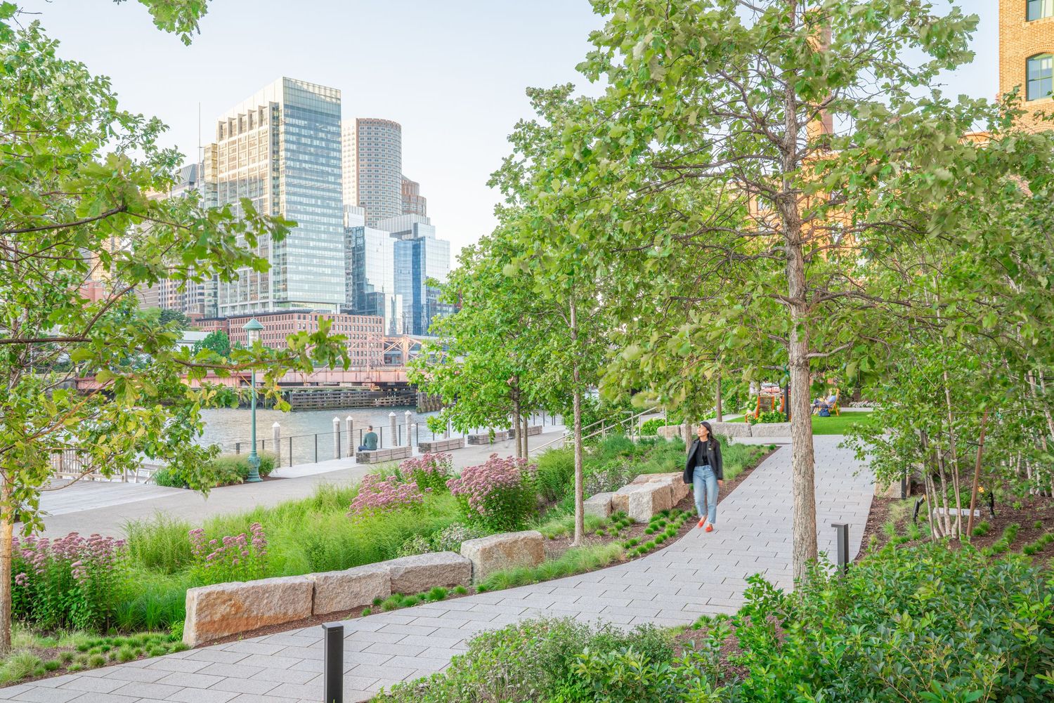 Green urban pathway with native plants and downtown skyscrapers visible in the background.