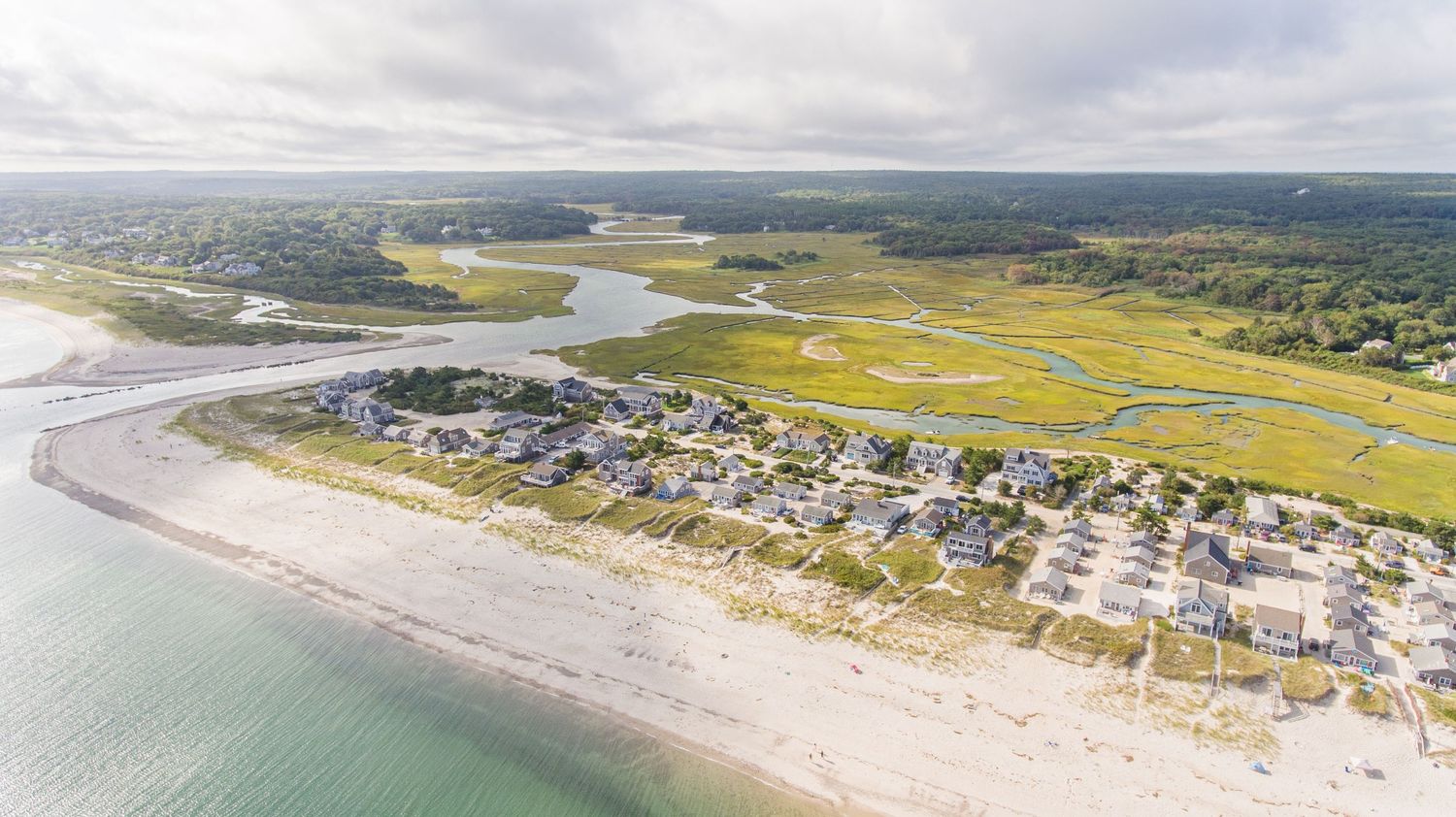 Aerial panoramic view of coastal town and beach with houses nestled along the shoreline.