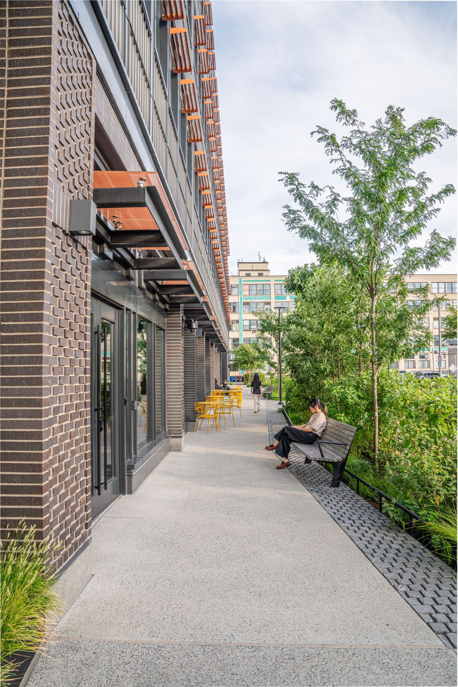 Modern brick building exterior with concrete walkway and landscaped garden elements.