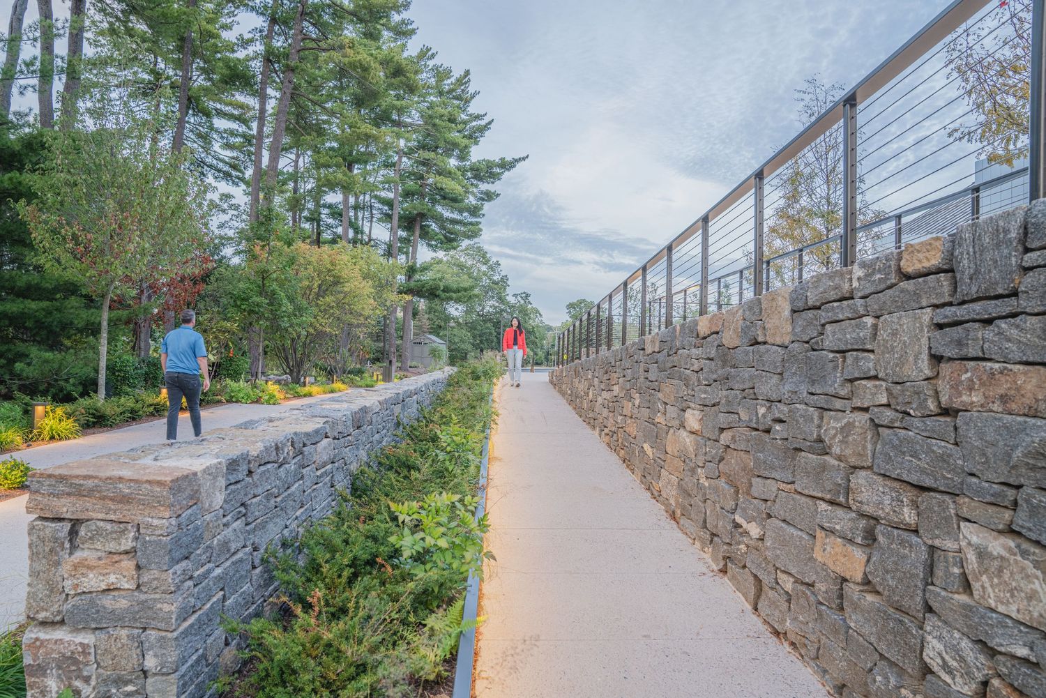 Long paved walkway with stone retaining wall and trees along the path.