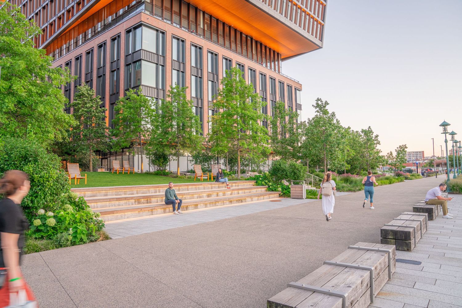 Public plaza space with benches and greenery near modern office buildings.