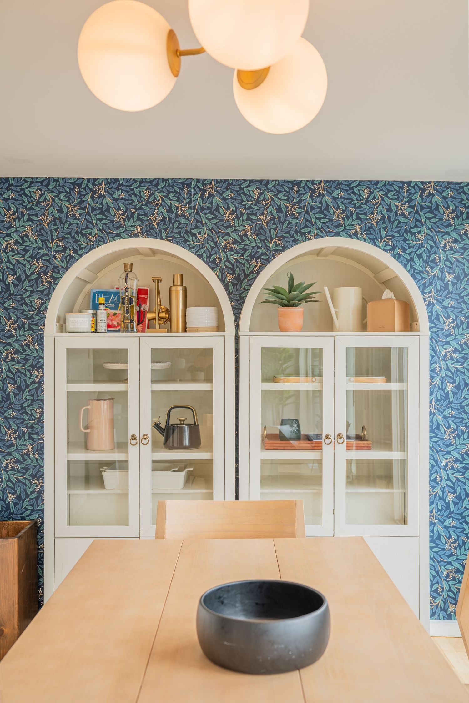Pro interior photography of modern dining room features arched glass cabinets with blue floral wallpaper and warm globe pendant lights