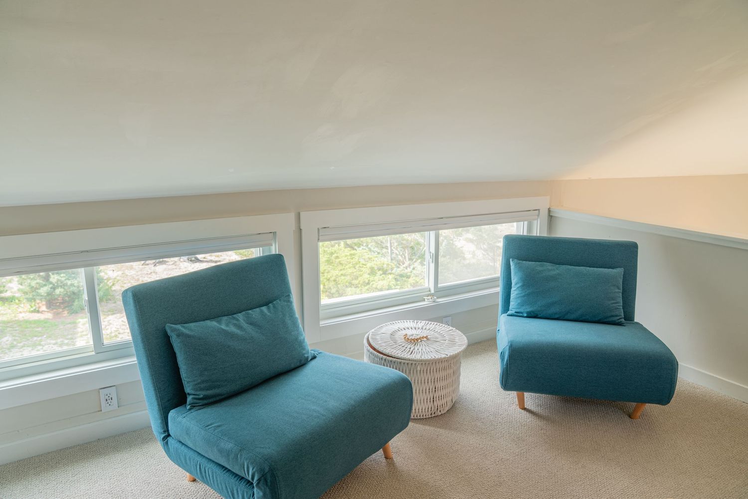Minimalist room with teal chaise lounges along sloped ceiling and large windows.