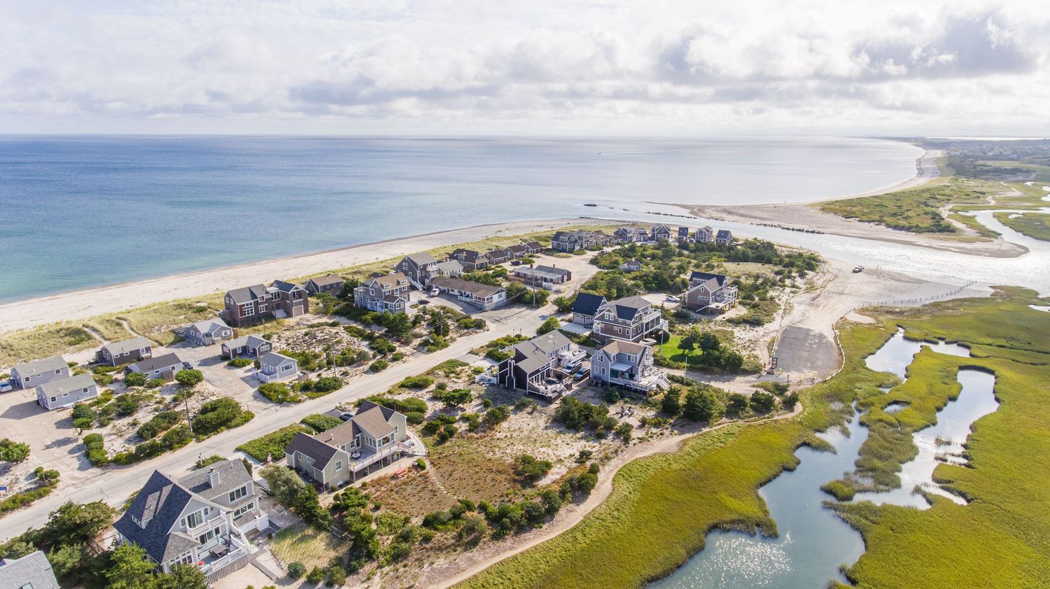 Aerial panoramic view of coastal homes and waterways along a scenic barrier island shoreline.