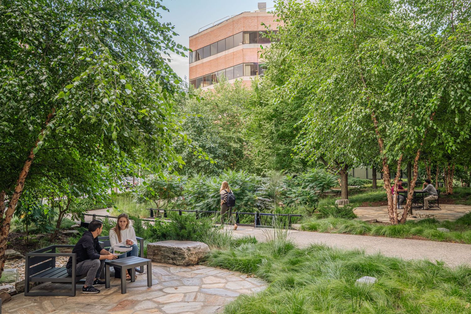 Urban park seating area with stone paving and lush greenery provides a peaceful gathering space.