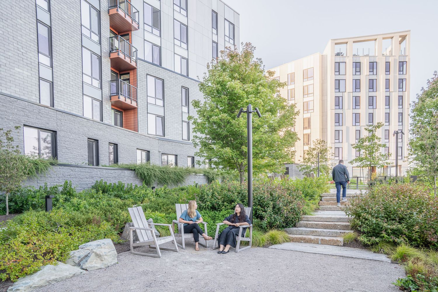 Winding concrete path between modern apartment buildings with landscaped grounds.