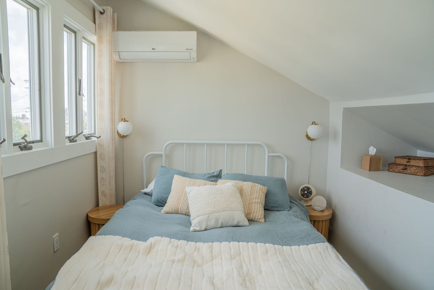 Cozy bedroom with slanted ceiling, wooden accents, and blue throw pillows on white bedding.