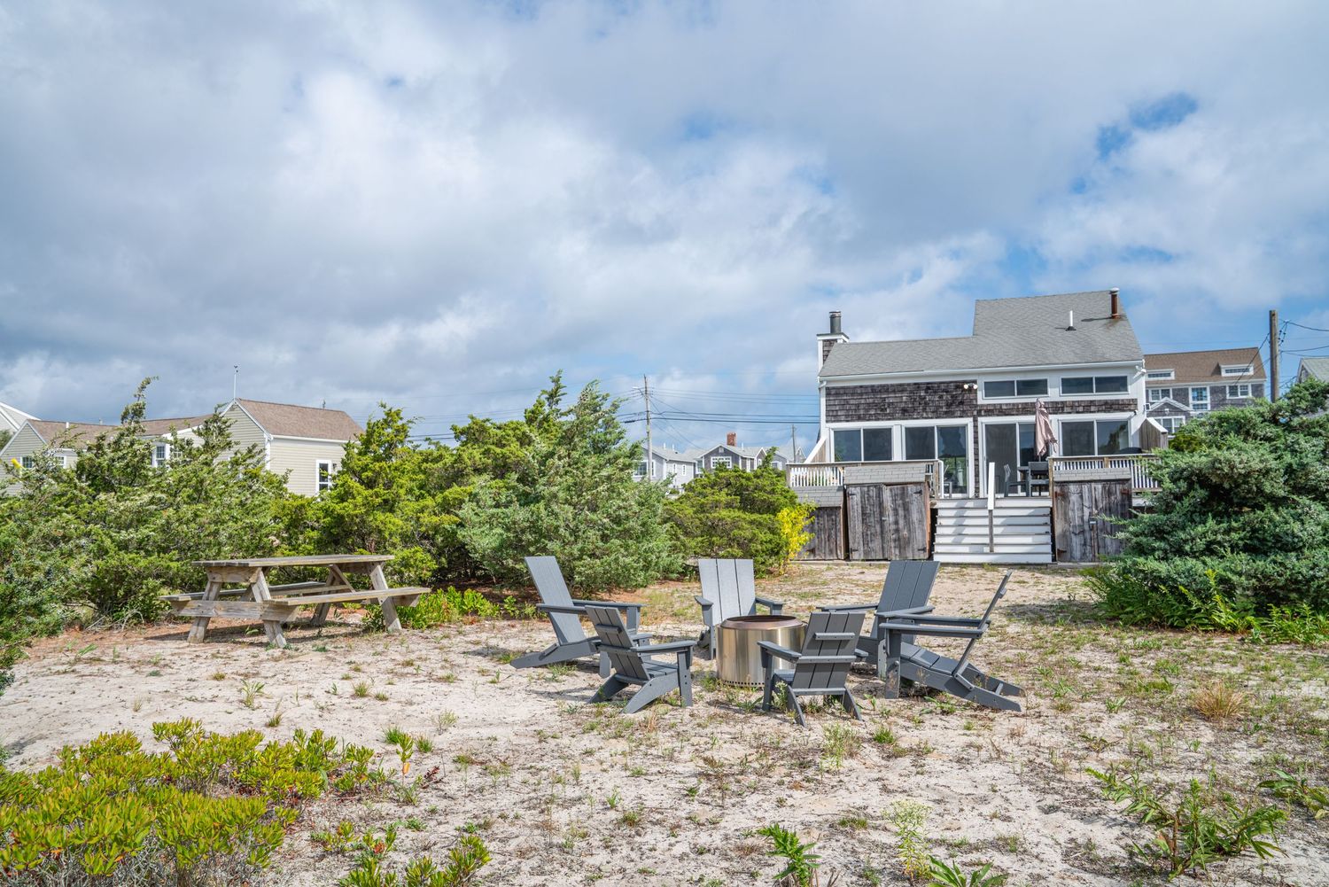 Beachfront property with Adirondack chairs overlooking sandy dunes and coastal vegetation.