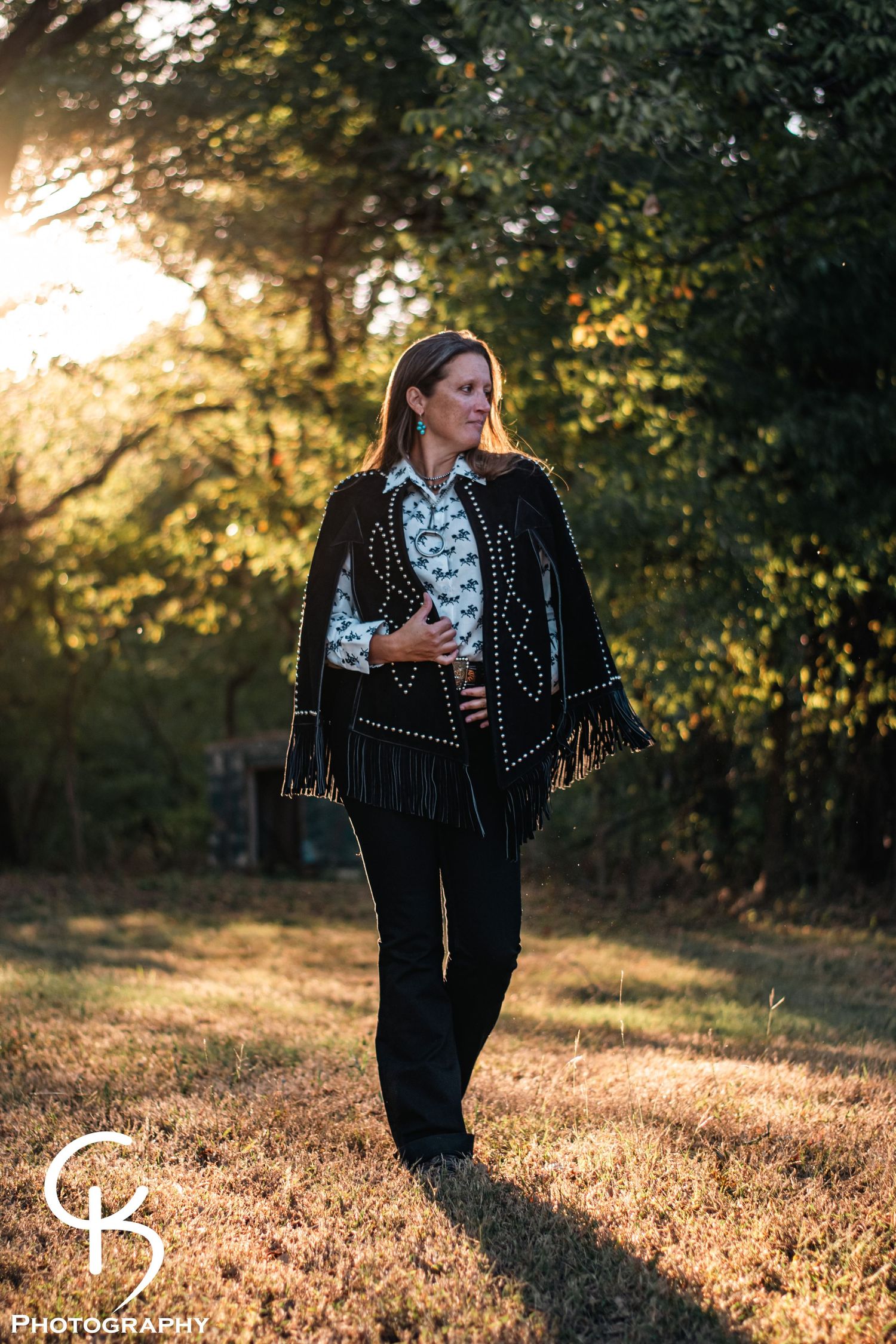 Western portrait photography of a woman in a fringed jacket, captured outdoors in golden hour light with warm rustic countryside atmosphere.