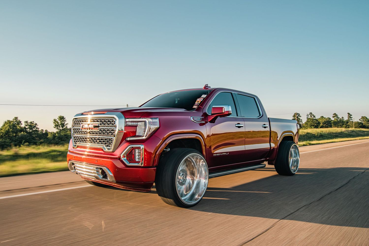 Rolling shot of a custom red GMC Sierra on chrome wheels, captured in golden hour light with bold detail and powerful street presence.