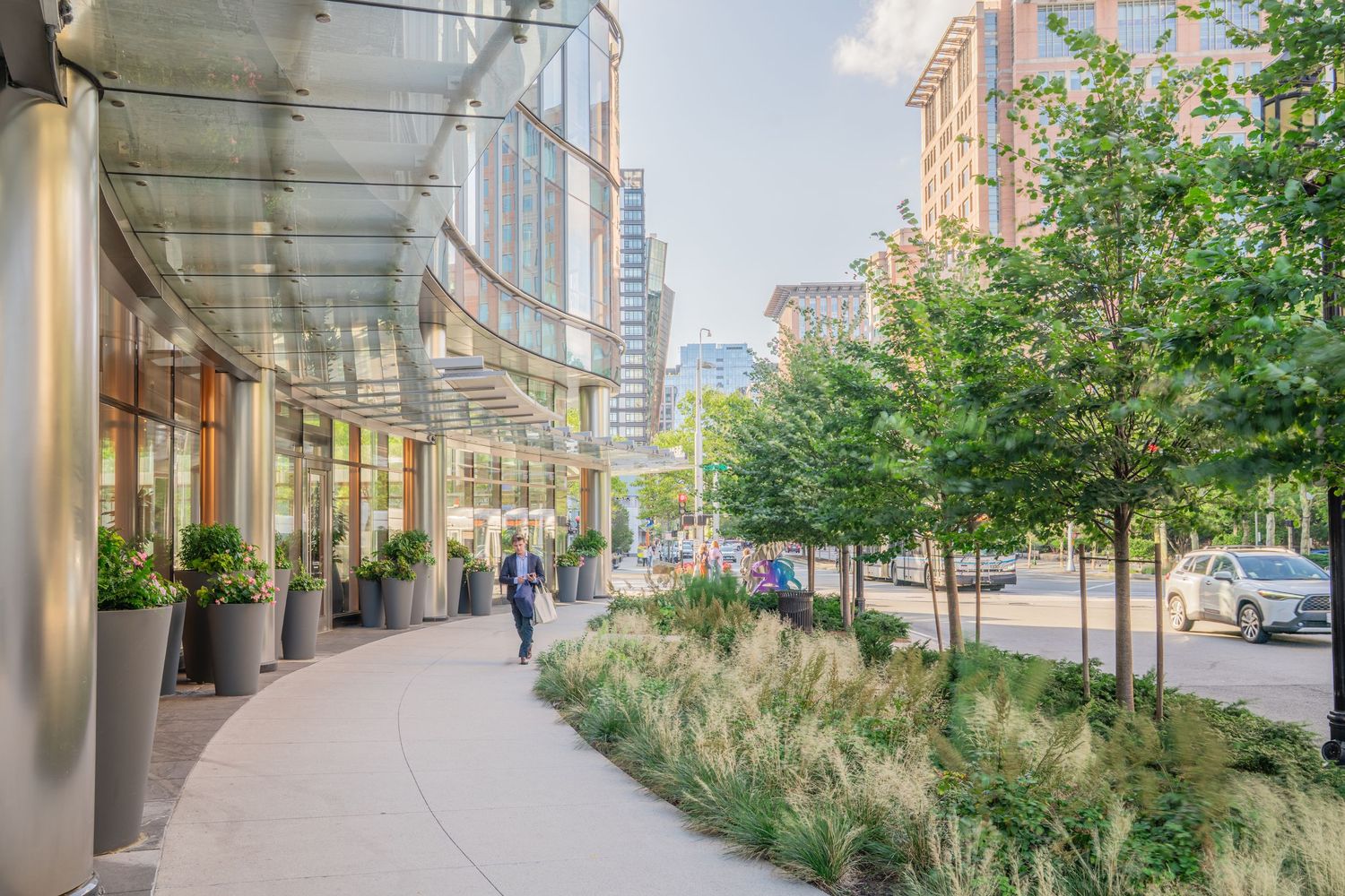 Urban sidewalk with green landscaping and tall buildings in the background.