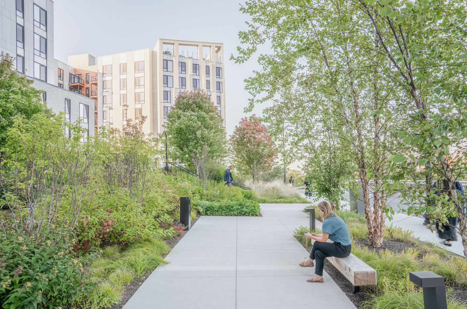 Landscaped courtyard between modern apartment buildings with benches and walking paths.