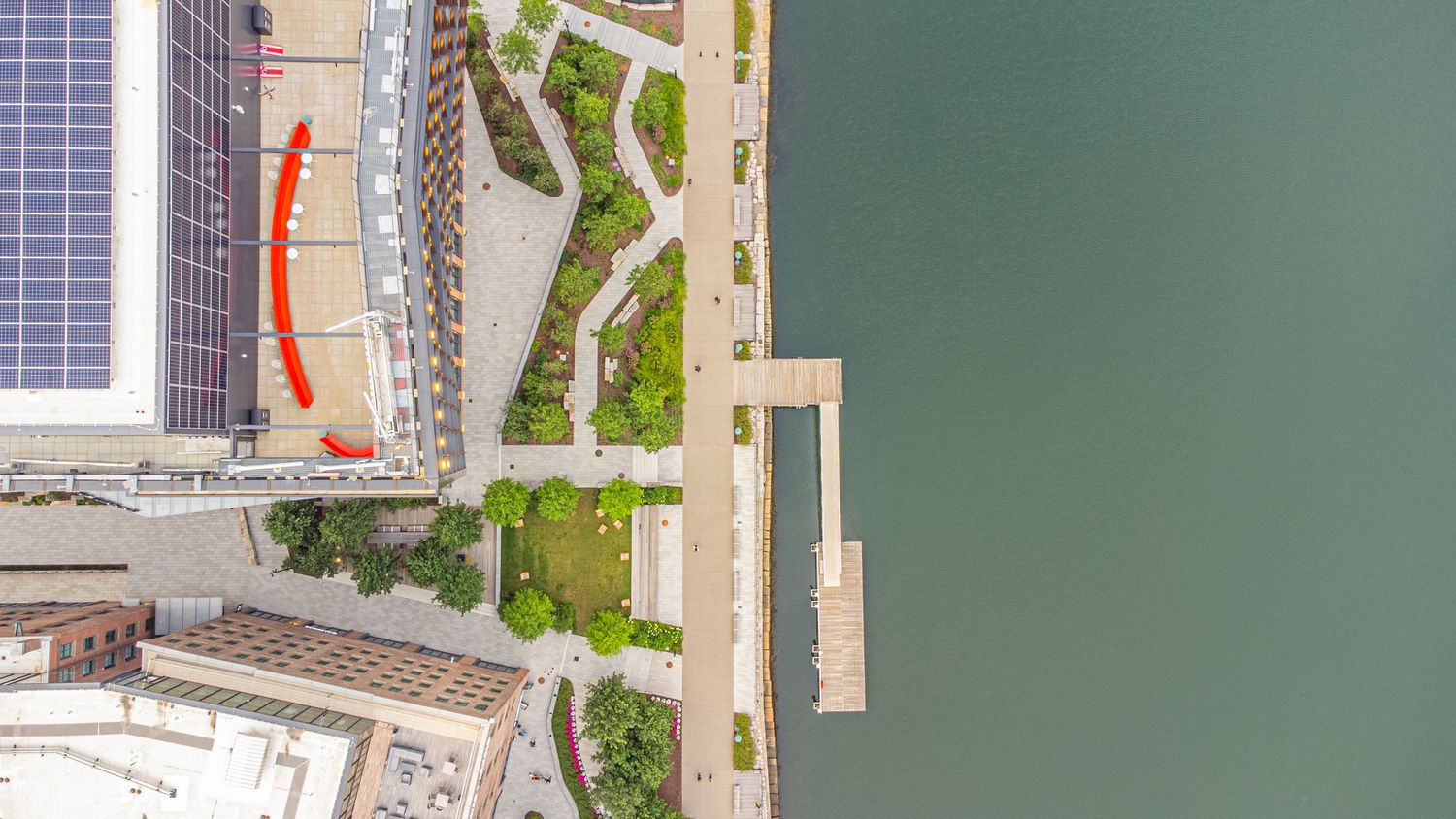 Aerial view of a modern waterfront development with green spaces and walkways along the shoreline.