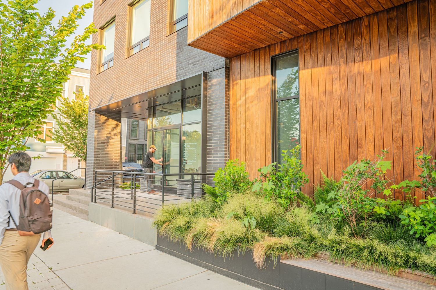 Contemporary building facade with wood paneling and landscaped walkway.
