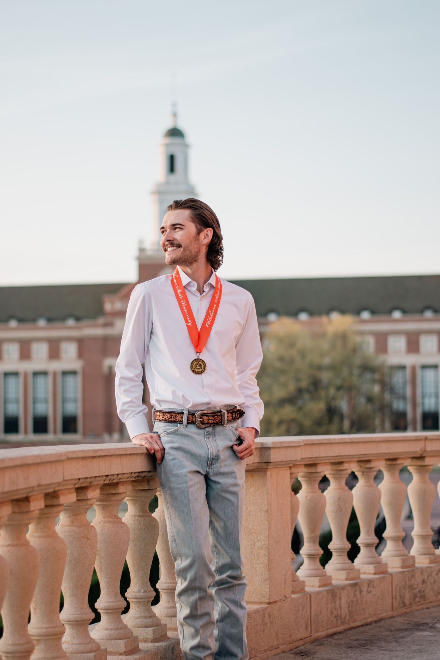 Graduation portrait photography of a young man with medal, captured in natural light with campus architecture as a timeless backdrop.