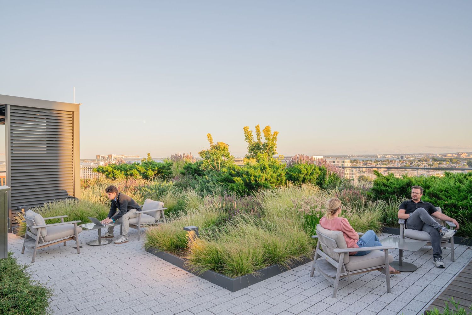 Outdoor seating area on rooftop deck surrounded by landscaped gardens at sunset.