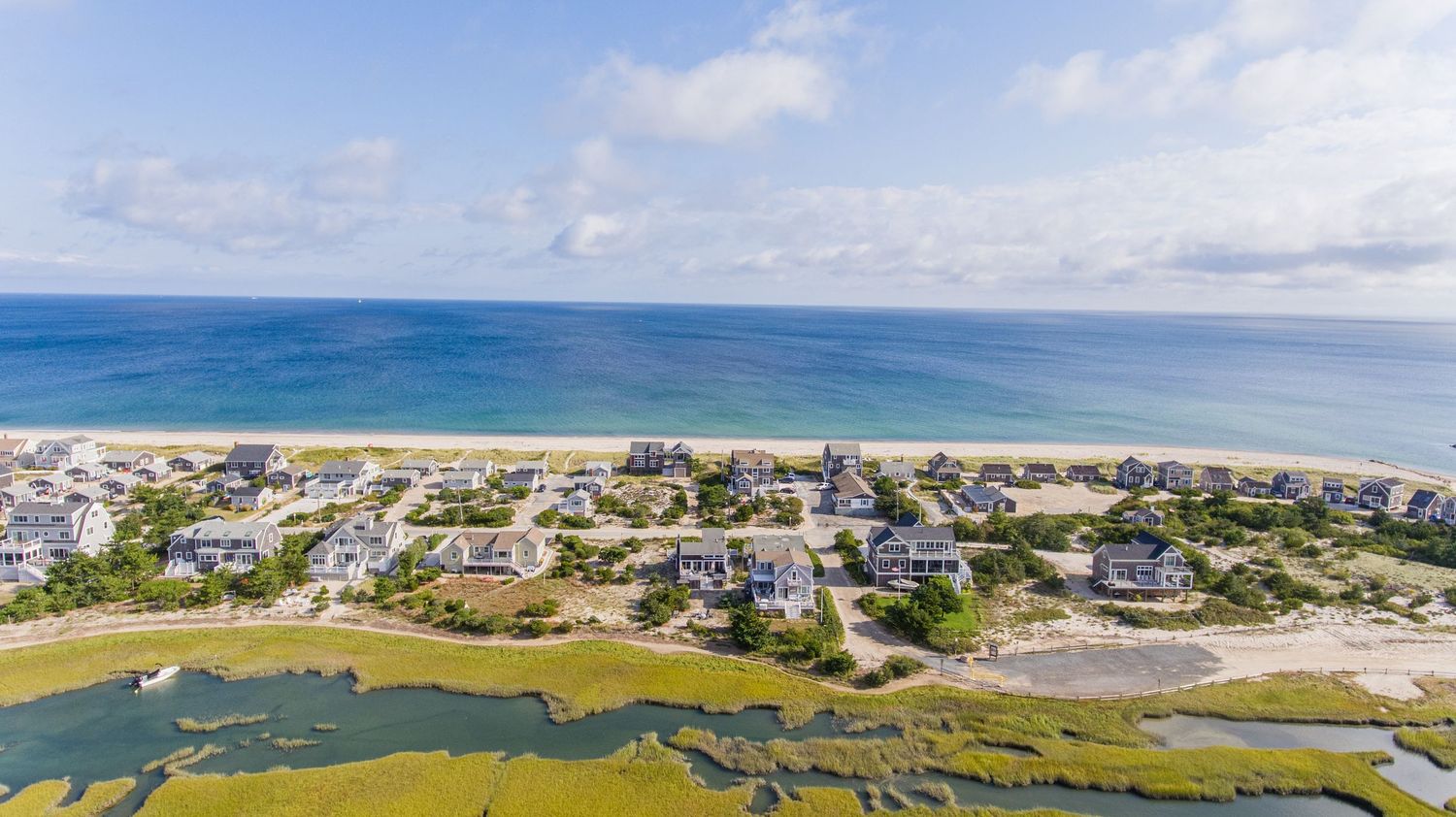 Panoramic aerial view of a coastal town with beachfront homes, sandy shores, and ocean waters stretching to the horizon.