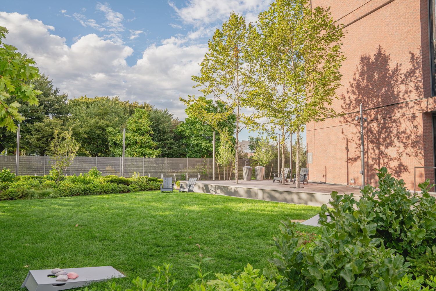 Modern urban landscaping features paved walkways and green spaces between brick buildings on a sunny day.