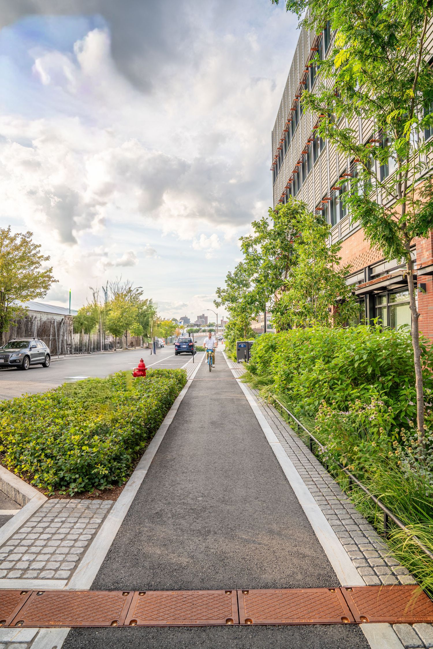 Urban walkway with landscaped greenery and modern buildings featuring paved paths and decorative concrete elements.