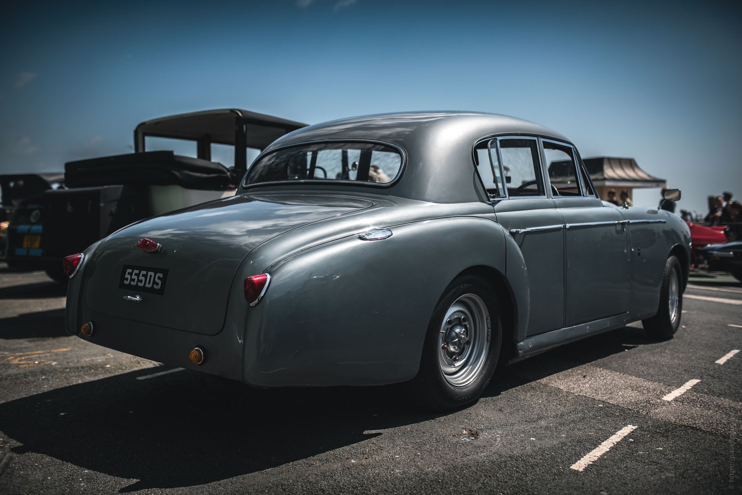 A vintage silver sedan parked on a sunny day, showcasing its classic rear design and sleek lines.