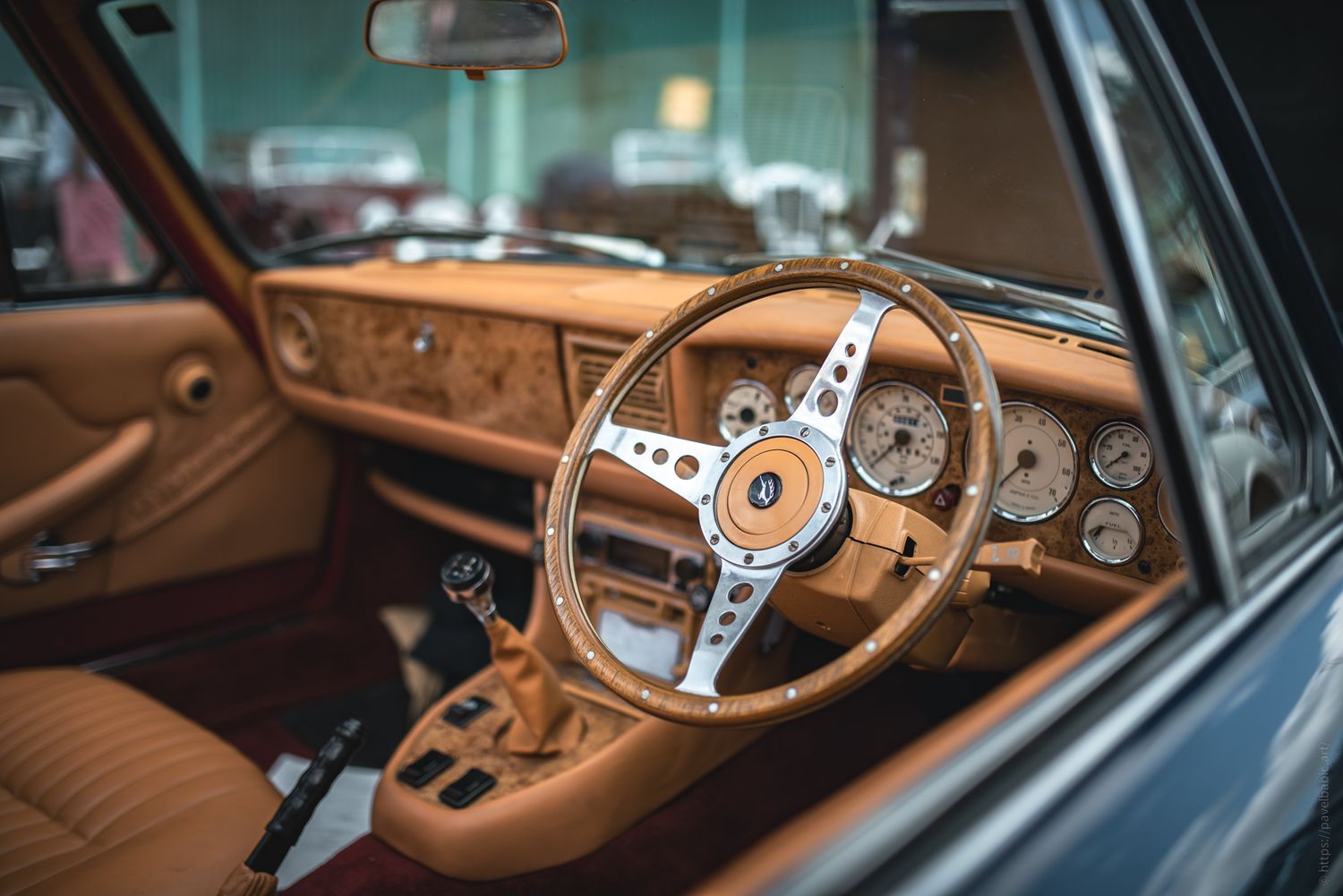 Interior of a classic car featuring a wooden steering wheel and vintage dials against a tan leather dashboard.