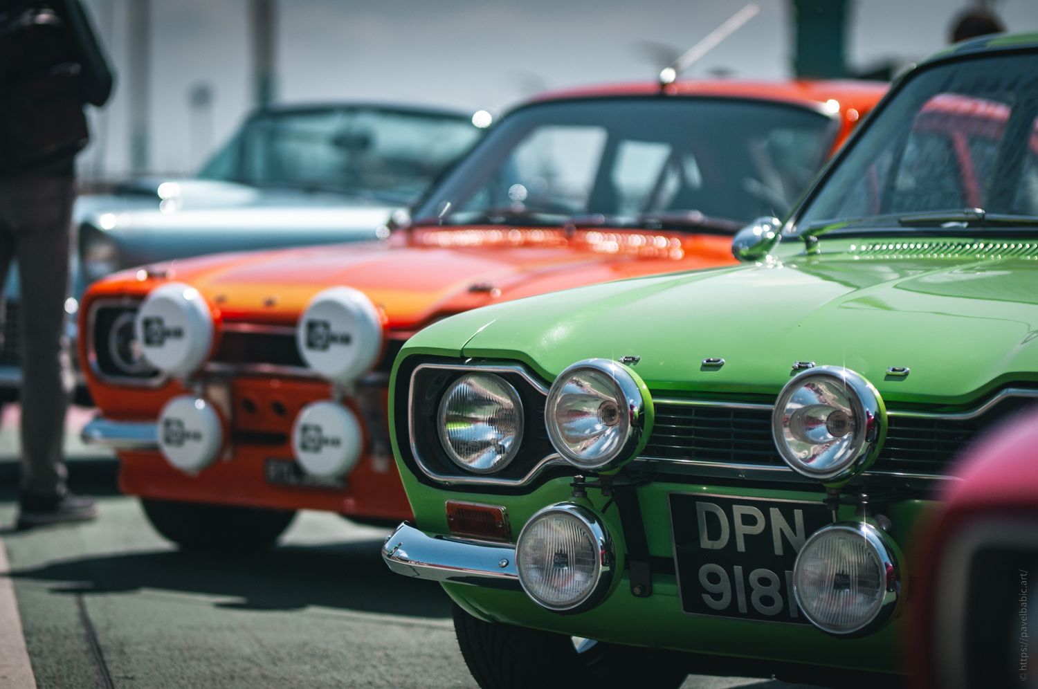 A close-up of vintage cars in vibrant colors—green, orange, and silver—showcasing classic designs and bright headlights.