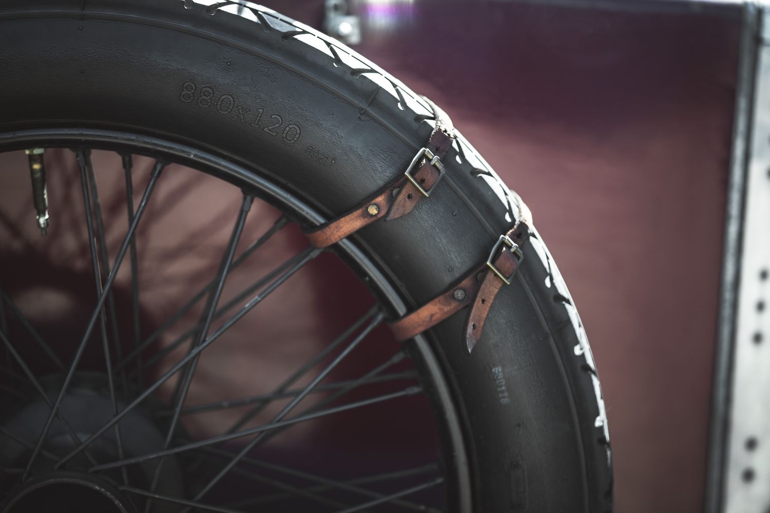 Close-up of a bicycle tire secured with leather straps, set against a blurred dark purple background.