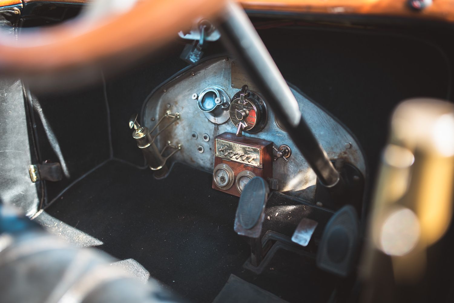 Close-up view of the footwell and dashboard in a vintage car, showing metal pedals, wiring, and mechanical components.
