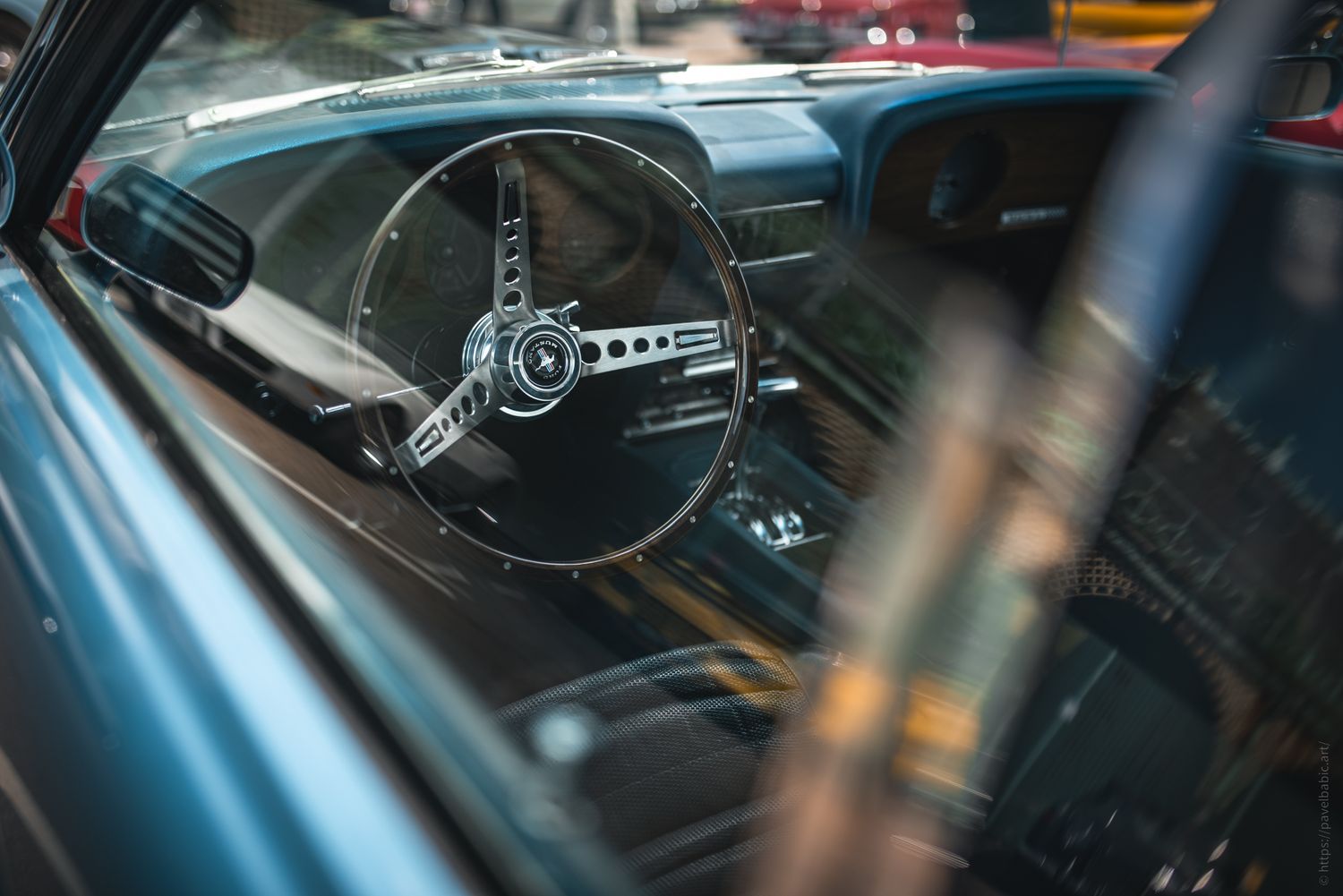 Close-up of a vintage car's steering wheel, showcasing its classic design through a slightly reflective windshield.