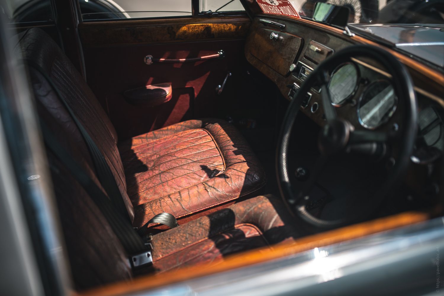 Interior of a vintage car featuring plush leather seats, a wooden dashboard, and classic gauges, bathed in warm sunlight.