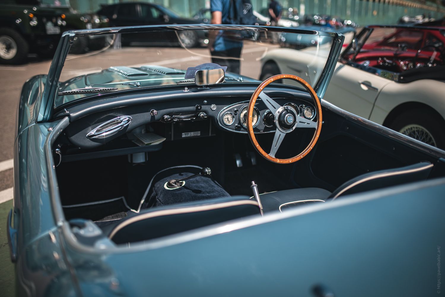 Interior of a classic convertible car featuring a wooden steering wheel, sleek dashboard, and open-top view.