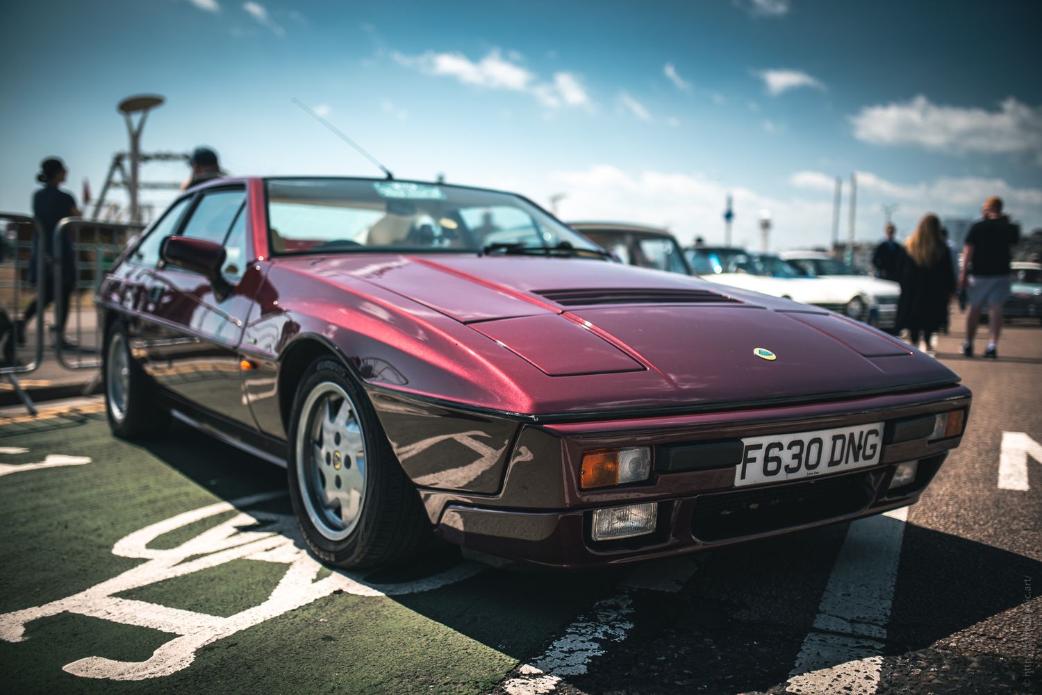 A sleek, burgundy 1980s sports car parked in a sunny outdoor area, showcasing its distinct design and classic style.