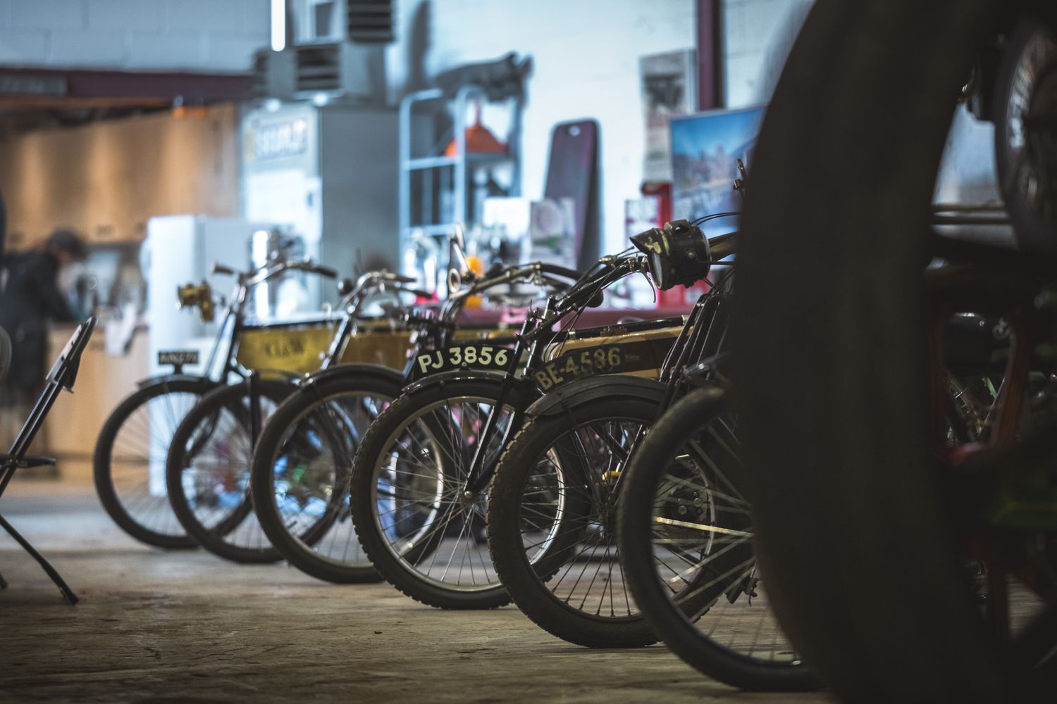 A row of vintage bicycles lined up in a garage, showcasing unique designs and colorful frames against a soft, industrial backdrop.