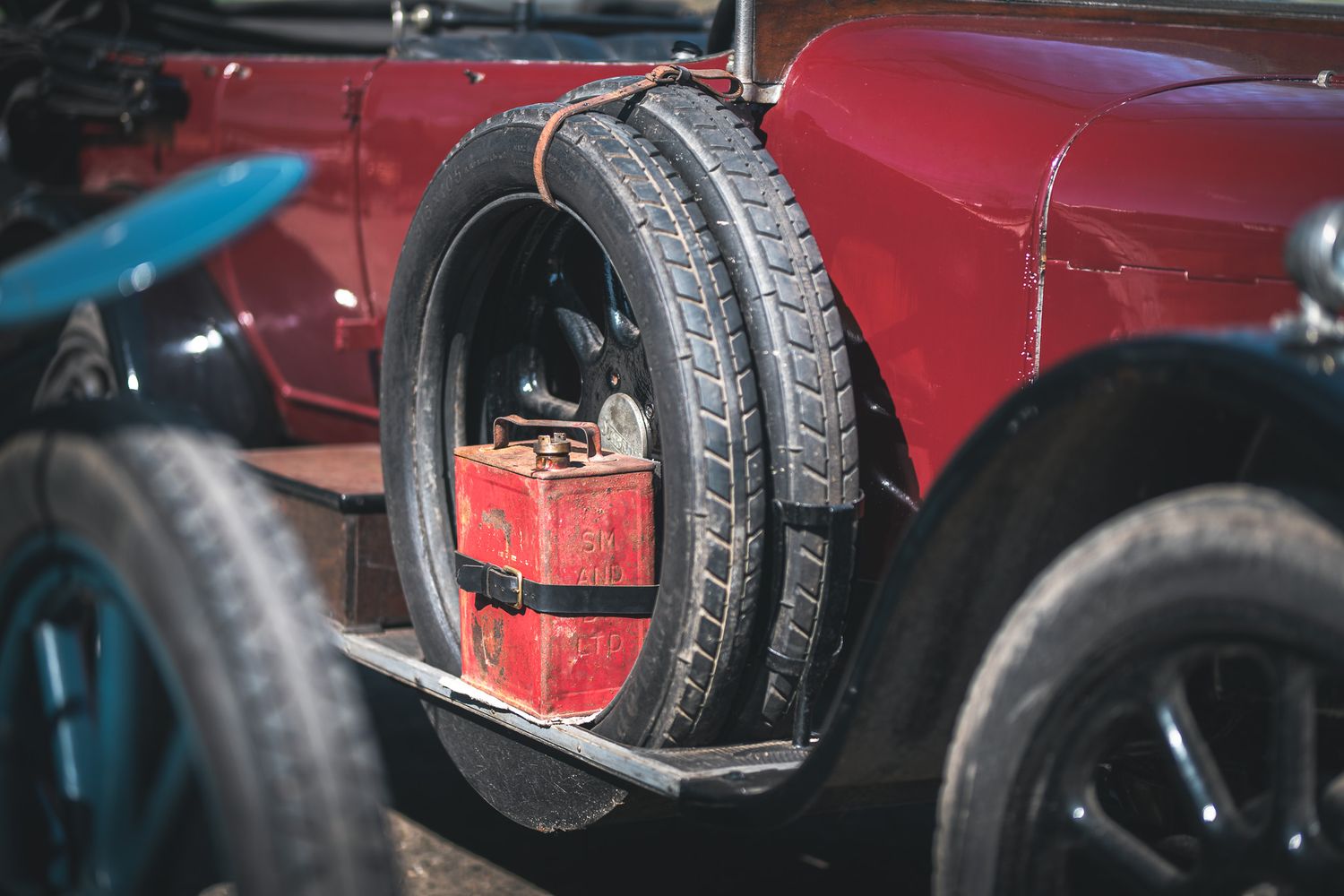 A vintage red car's rear showcases a spare tire and a small red toolbox, reflecting classic automotive design.