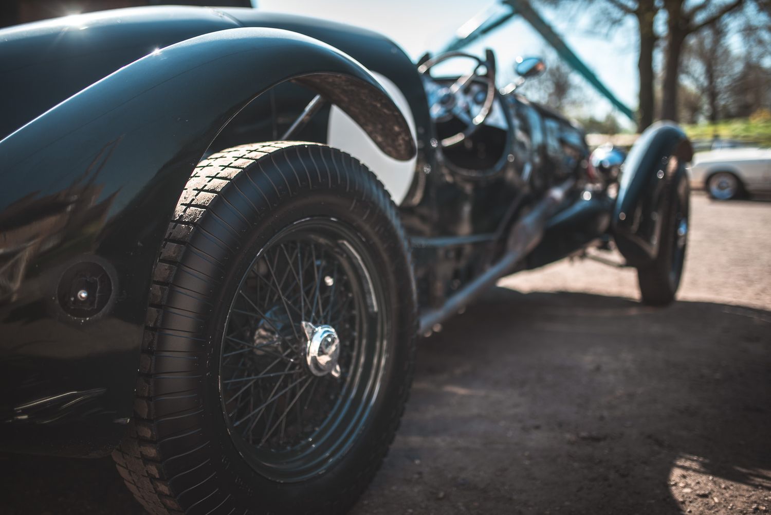 A close-up view of a classic black vintage car, showcasing its wire-spoke wheel and sleek curves under bright sunlight.