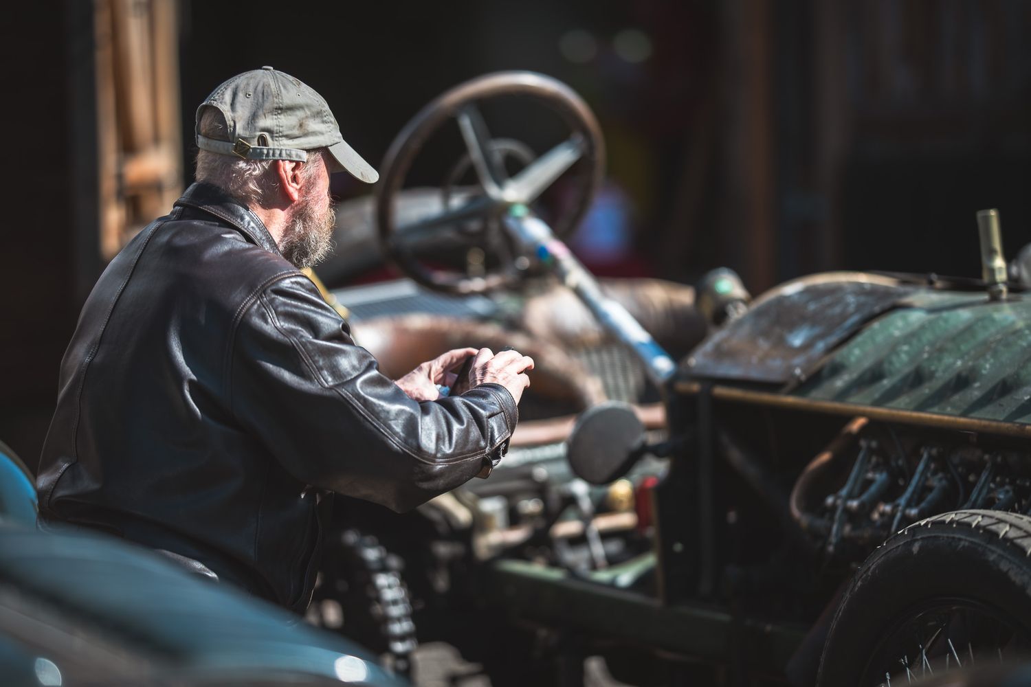 An older man in a cap inspects the engine of a vintage tractor, showcasing craftsmanship and nostalgia in a sunlit workshop.