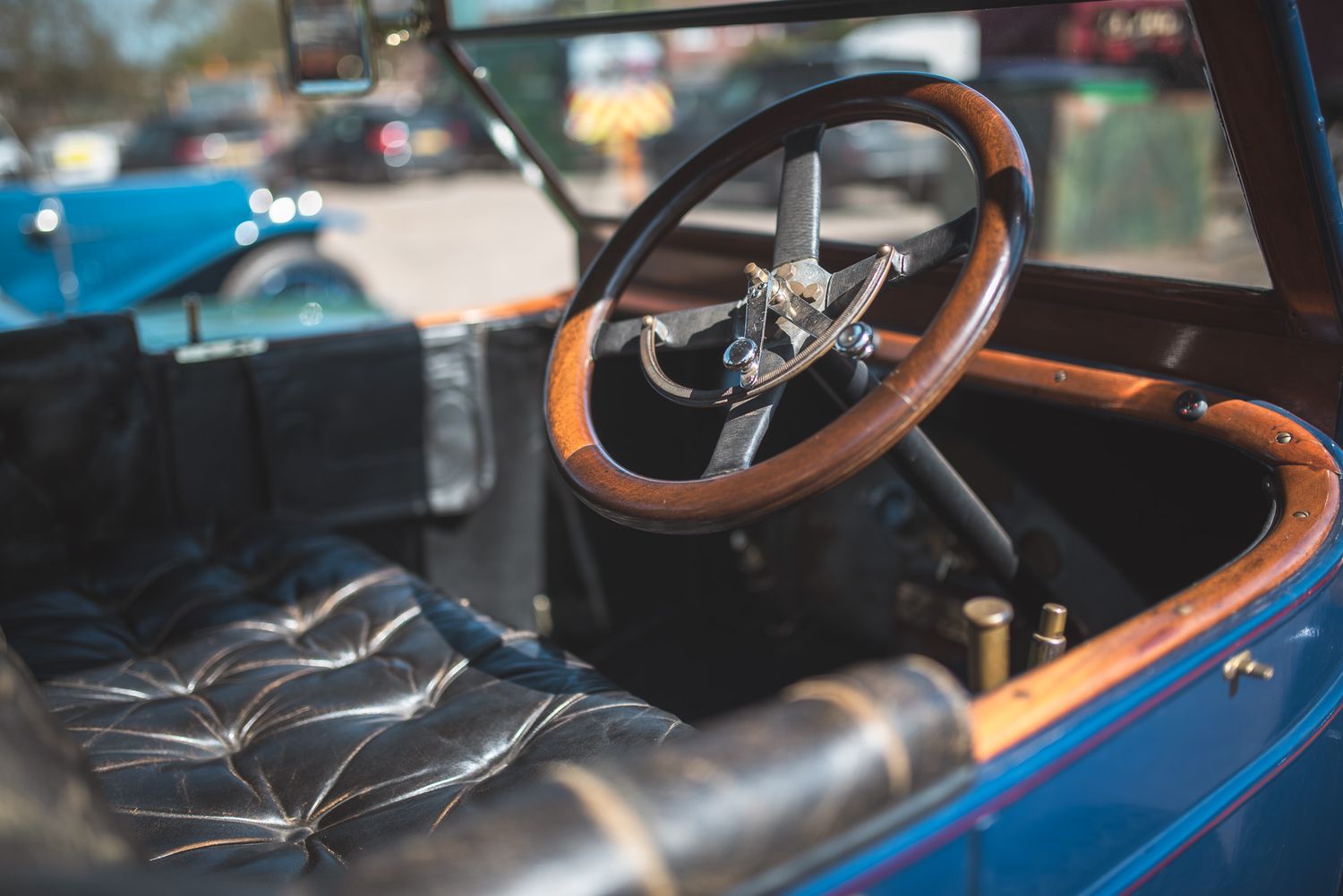 Close-up of a vintage car's wooden steering wheel and dashboard, with a blurred crowd in the background, creating a nostalgic and classic at