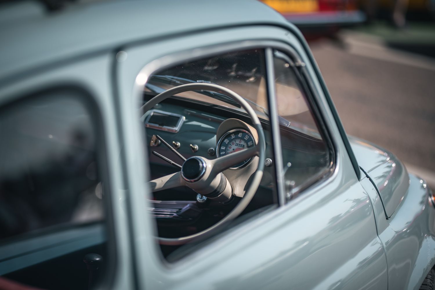 Close-up view of a vintage car's interior, featuring a classic steering wheel and dashboard through the driver's side window.