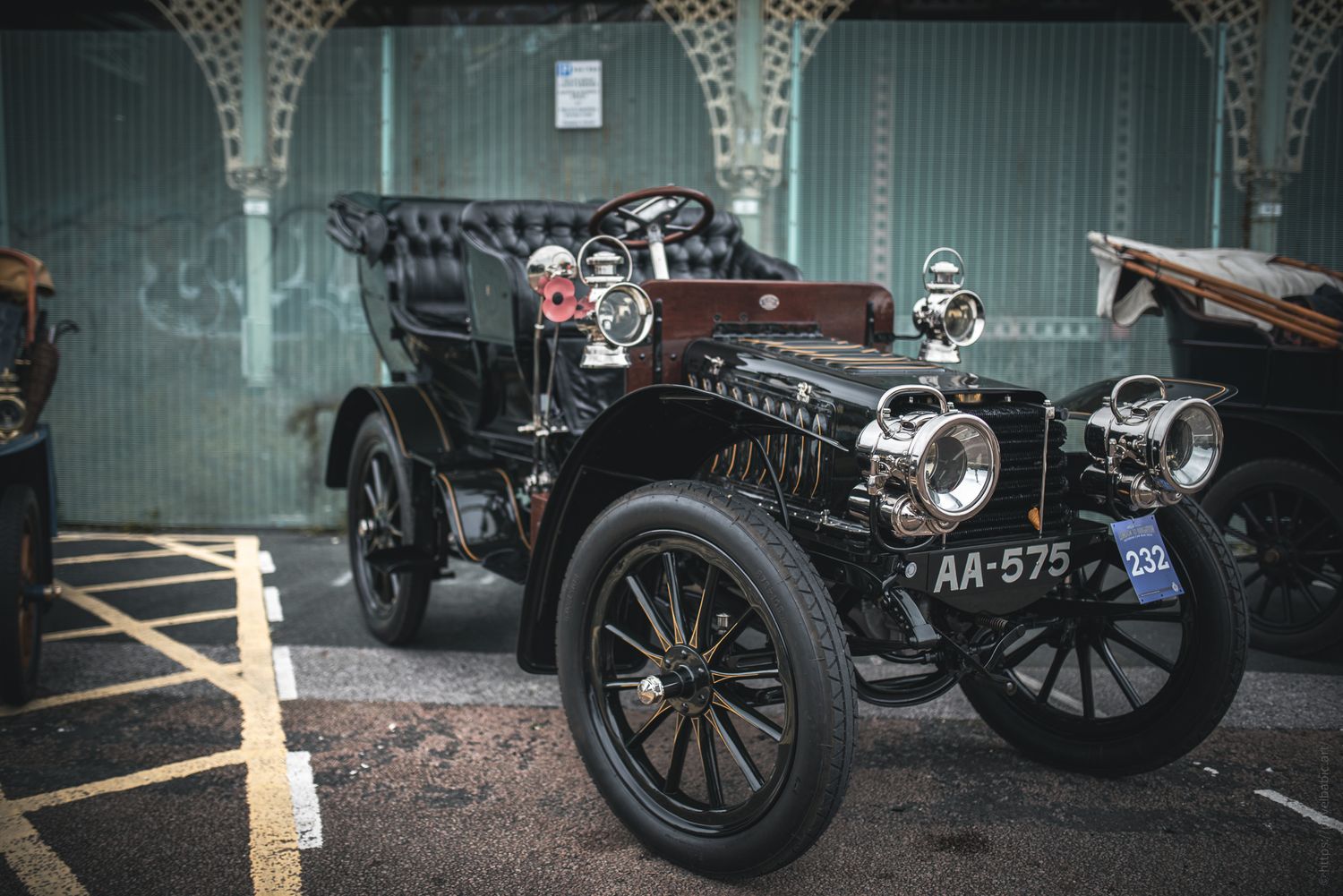 A vintage black car from the early 1900s parked, featuring ornate headlights, a plush interior, and a classic design.