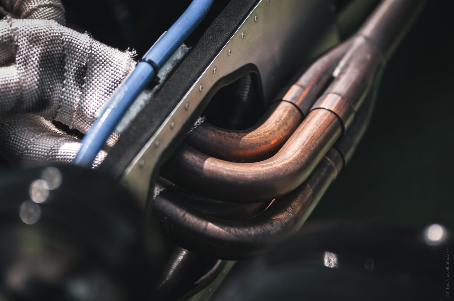 Close-up of metal exhaust pipes with a blue wire nearby, showcasing intricate industrial design and connecting components.