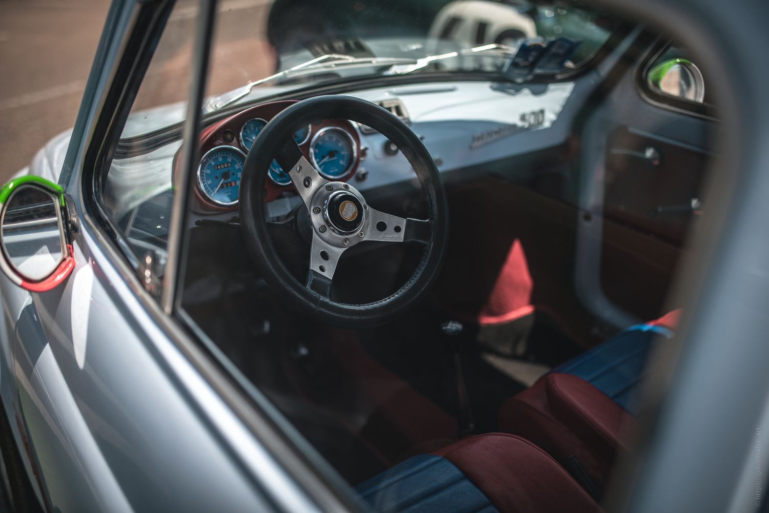 Interior view of a classic car featuring a sleek steering wheel, colorful gauges, and stylish red and blue upholstery.
