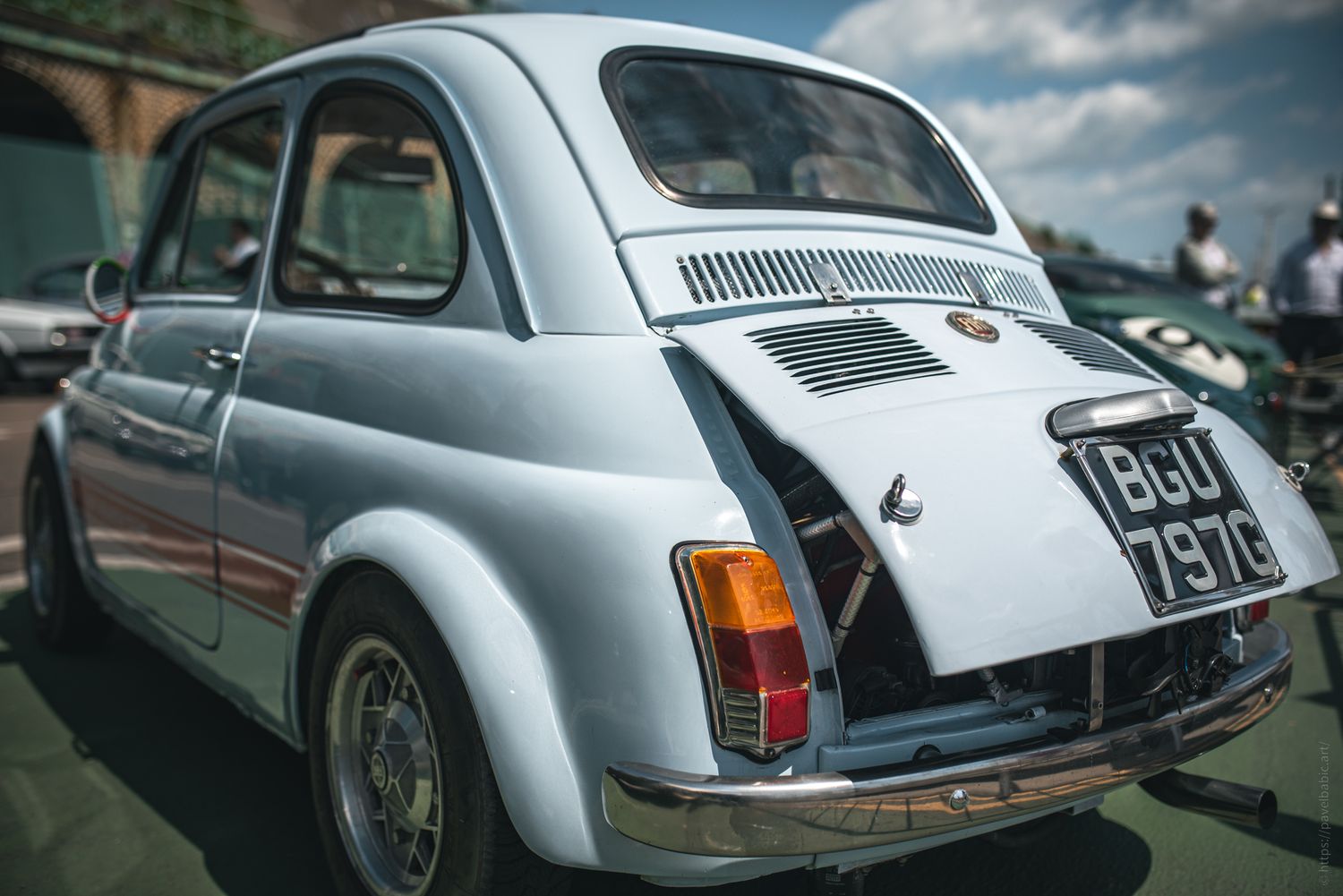 Light blue classic car with an open engine compartment, showcasing its vintage style and charm under a clear blue sky.