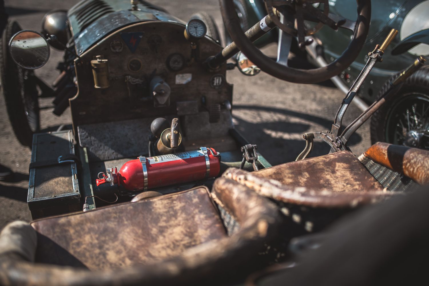 Close-up of an antique car's interior, featuring weathered leather seats, a dashboard with gauges, and a red fire extinguisher. 1913 Monarch