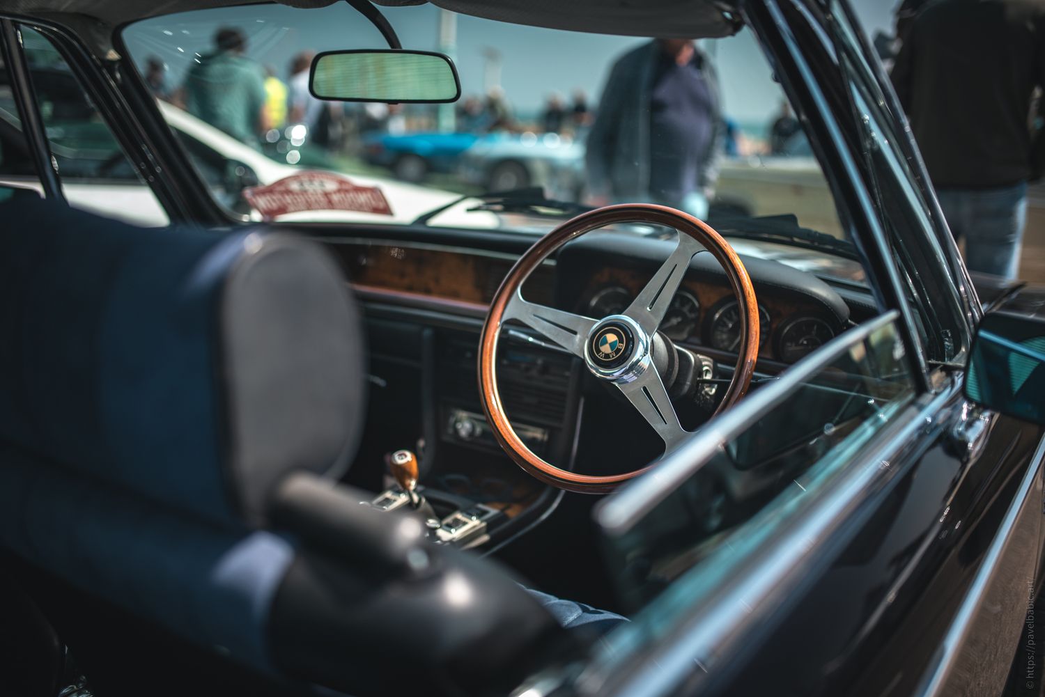 A classic car interior featuring a wooden steering wheel, plush seats, and a detailed dashboard with vintage design elements.