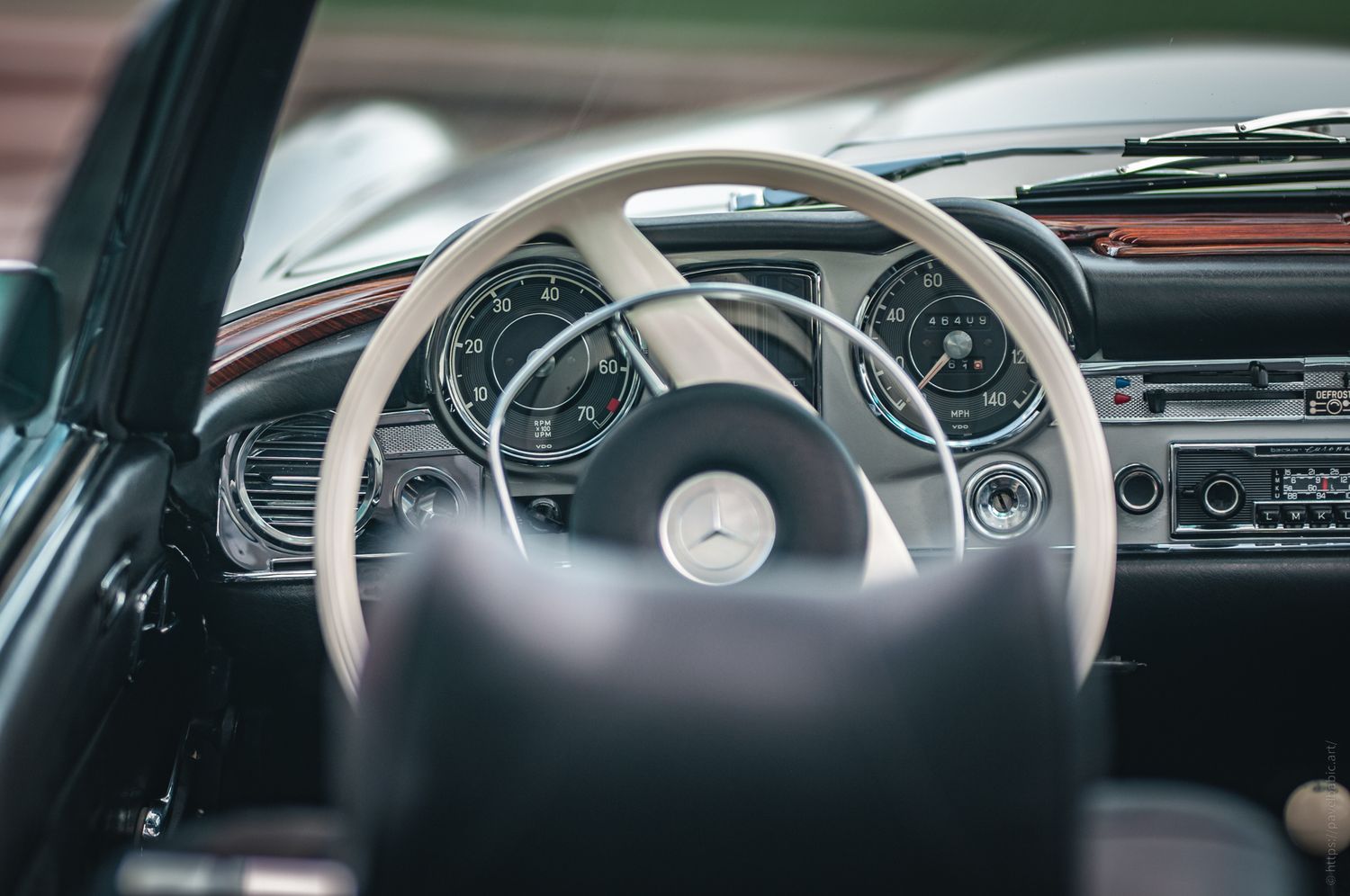 The interior of a classic Mercedes-Benz, featuring a stylish white steering wheel and vintage dashboard with dual gauges.